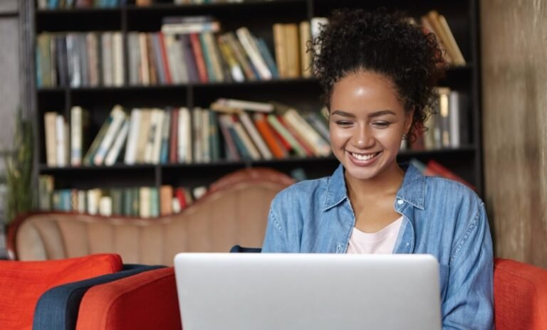 Estudante sorrindo diante de notebook em biblioteca